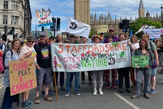 A large group of people hold a banner that says Staffordshire Votes for Nature with Big Ben in the skyline behind them, a blue sky with thin cloud overhead