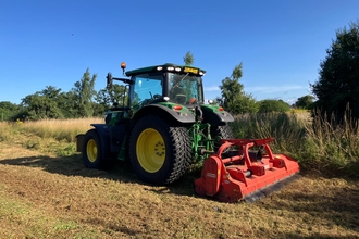 a tractor works on a sunny day mowing high grass.