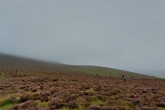 An open expanse of moorland with people in the far distance. The sky is grey and murky with mist hanging over the moorland.