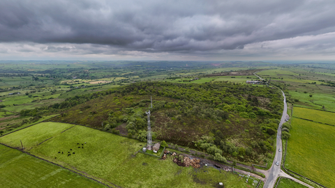 An aerial shot of an expanse of woodland and heathland among a landscape of green farmland, with grey clouds overhead.