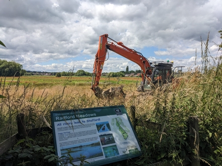 A digger makes passes by an interpretation board on a nature reserve under a cloudy sky