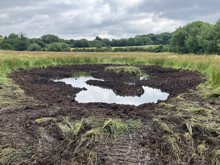 A freshly dug pond in a field begins to fill with water.