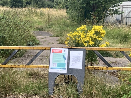 Signs on a stand in front of a gate to a local green space.