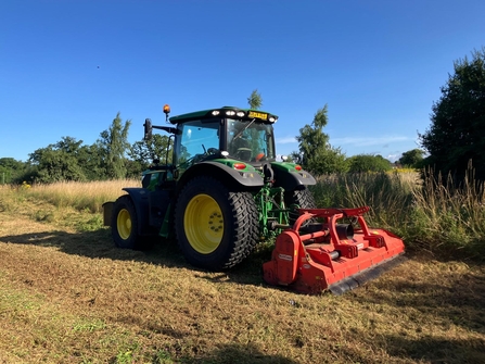 a tractor works on a sunny day mowing high grass.