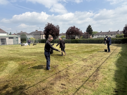A group of people sow seeds on a former tennis court